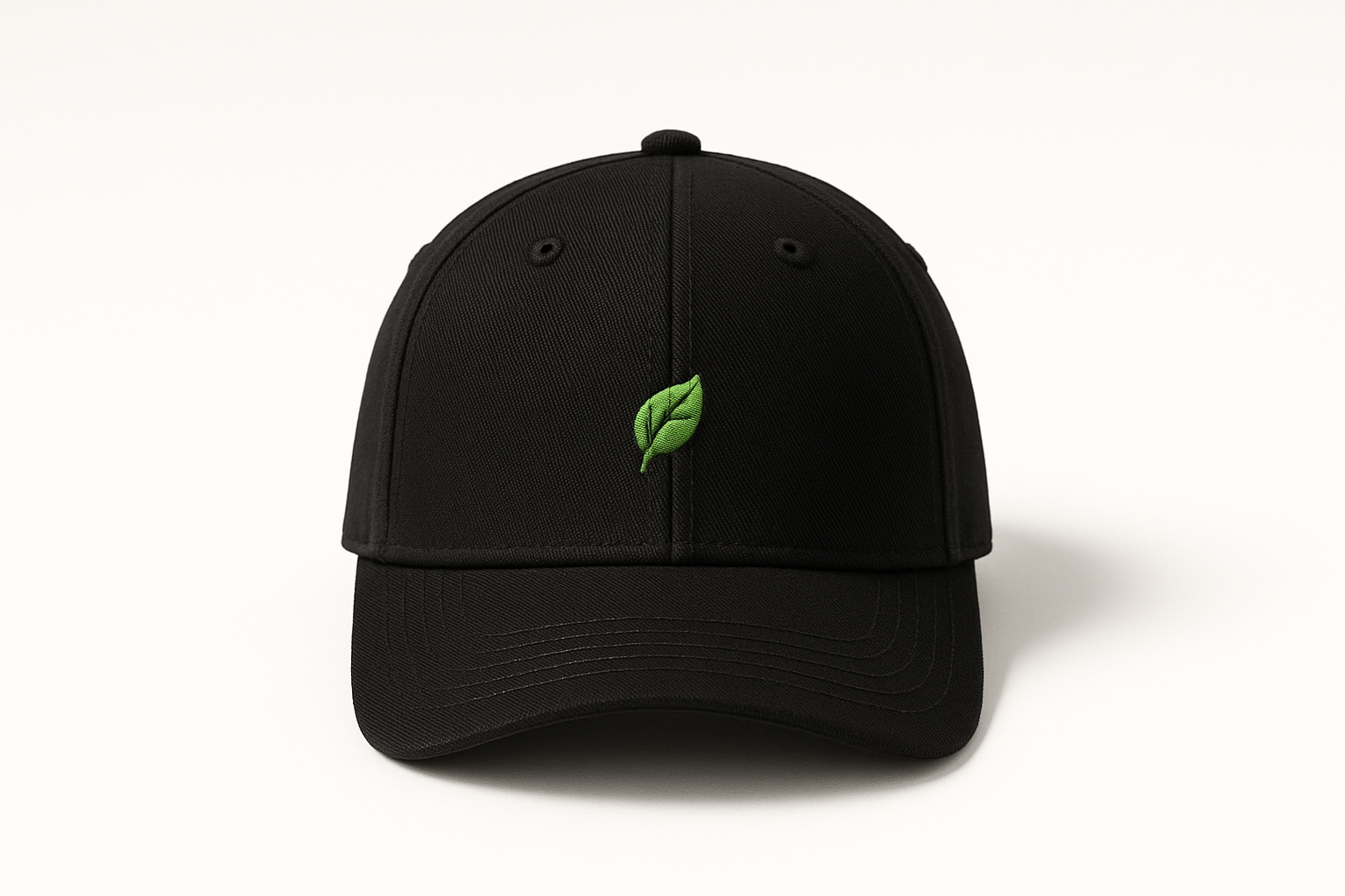 Freisteller einer schwarzen Cap aus Bio-Baumwolle, frontaler Blickwinkel, kleines gruenes Blatt-Icon als sauberer Stick vorne. Heller Studio-Hintergrund, weiche Schatten, scharfes Produktfoto, E-Commerce-Look, minimalistisch.